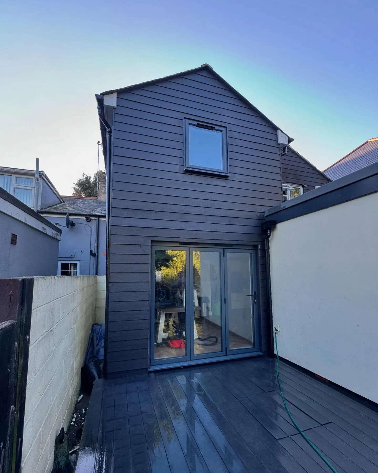 The finished two storey rear extension in dark cladding under a clear sky